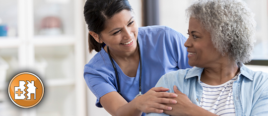 Female nurse leaning over a female patient with their hands touching.