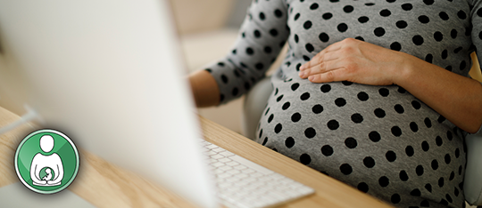 Pregnant person resting a hand across their stomach, while looking at a computer screen