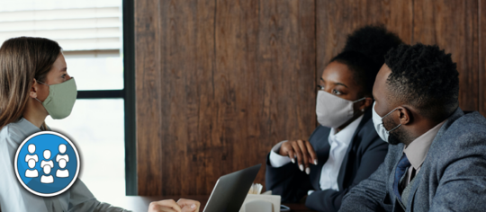 Three people wearing face masks talking around a table