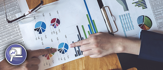 Hands of two people pointing at a pie chart on a sheet of various charts and figures.