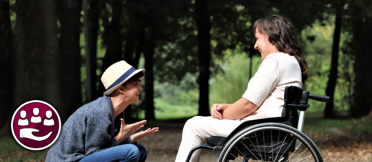 Person crouched down talking to person in a wheelchair.